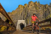 A man rides a bike on a wooden bridge near a mountain.