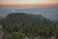 Sun rises over a valley with sequoia trees in the foreground.