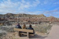 Three people sit on a bench looking out at an expanse of scenic badlands.