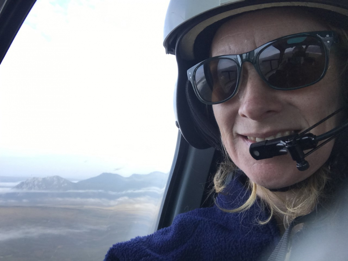 Woman in helicopter with mountain visible out window.