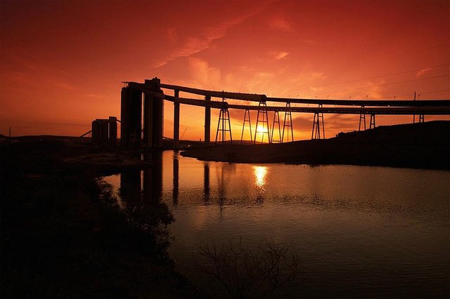 Coal operation structures silhouetted against an orange and red sunset.