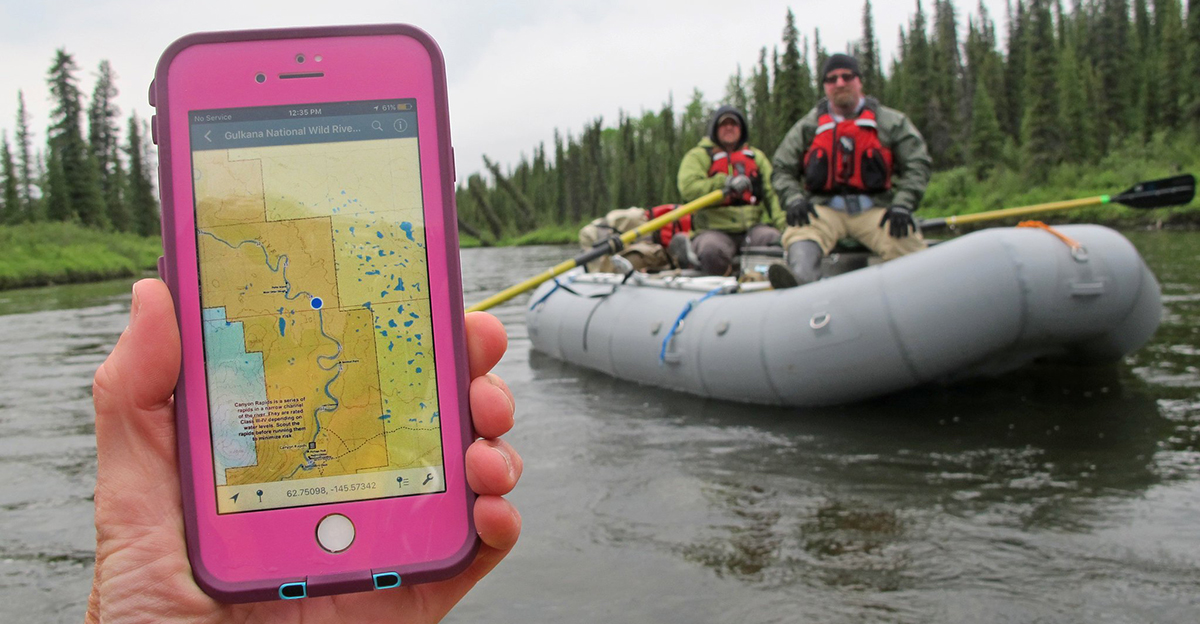 Floating the Gulkana Wild and Scenic river. Rafter holds up moblie device with georeferenced PDF map displayed with location dot showing where they are on the river.