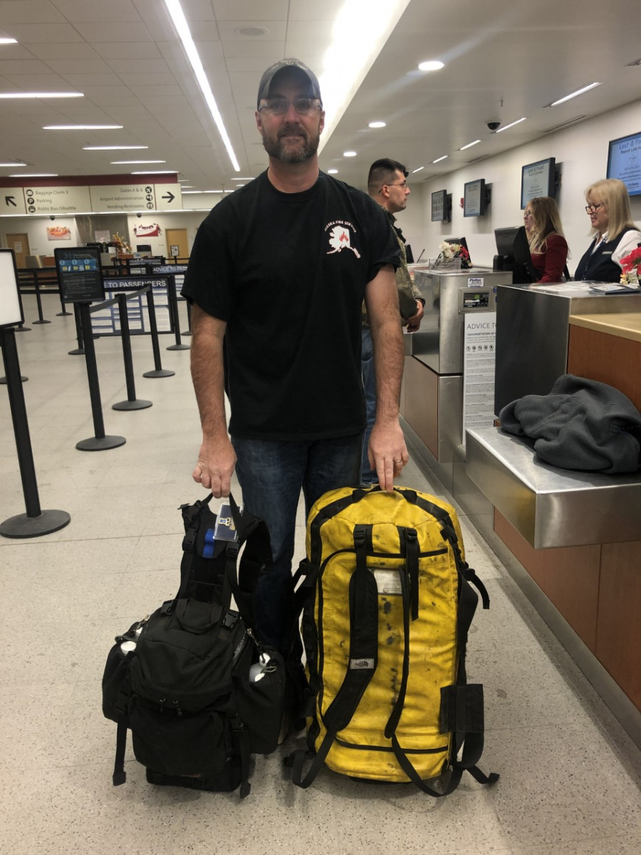 Firefighter Kyle Cowan standing with his gear in an airport.