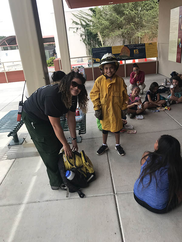 BLM Las Cruces District Outdoor Recreation Planner and Wildland Firefighter Edna Flores (right) lets a camp participant wear her gear.