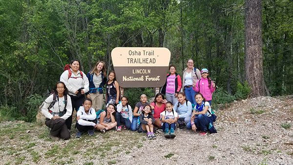 BLM staff Daniella Barraza (left kneeling), Courtney Platero (left standing), Amanda Munro (second to left standing) and Eileen Davis (right standing) and the girls pose before a hike in Cloudcroft, NM.