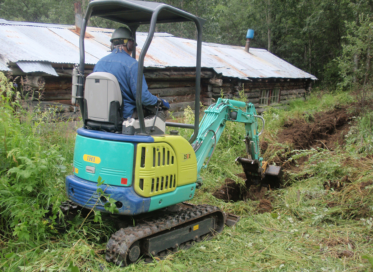 2012 Steele Creek townsite rehabilitation. Mini excavator digging trench near buildings