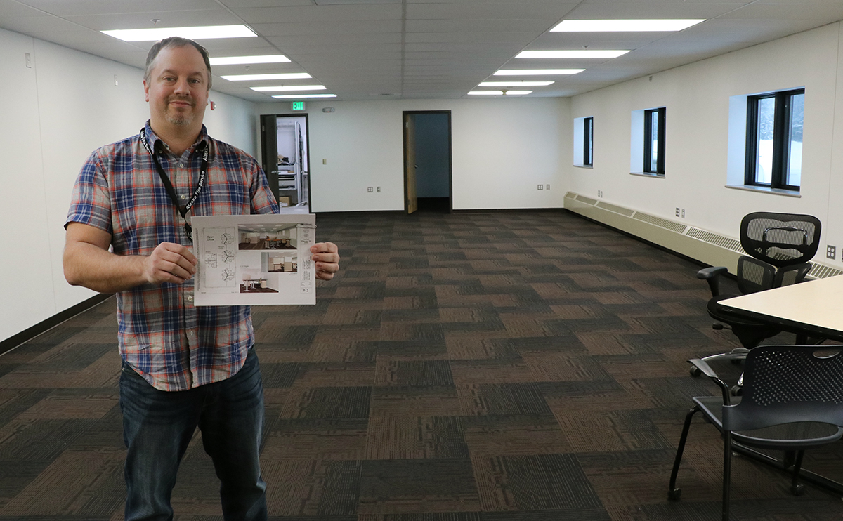 Man standing in empty room holding plans