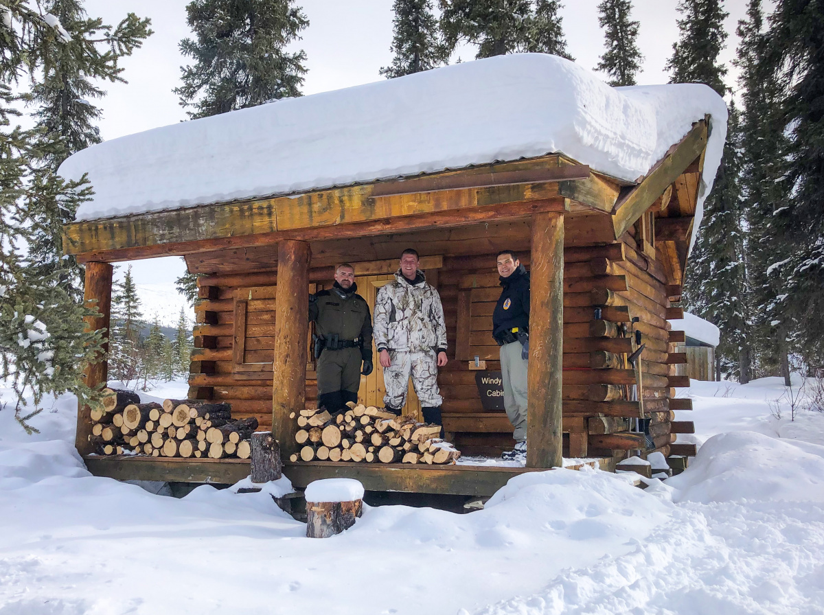 Three rescuers standing on the porch of a BLM public use cabin