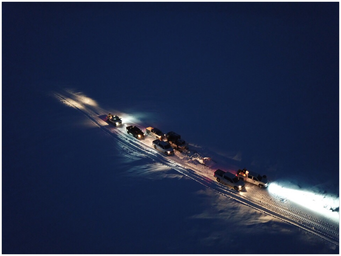 Aerial photo of people driving light vehicles on the snow road at night.