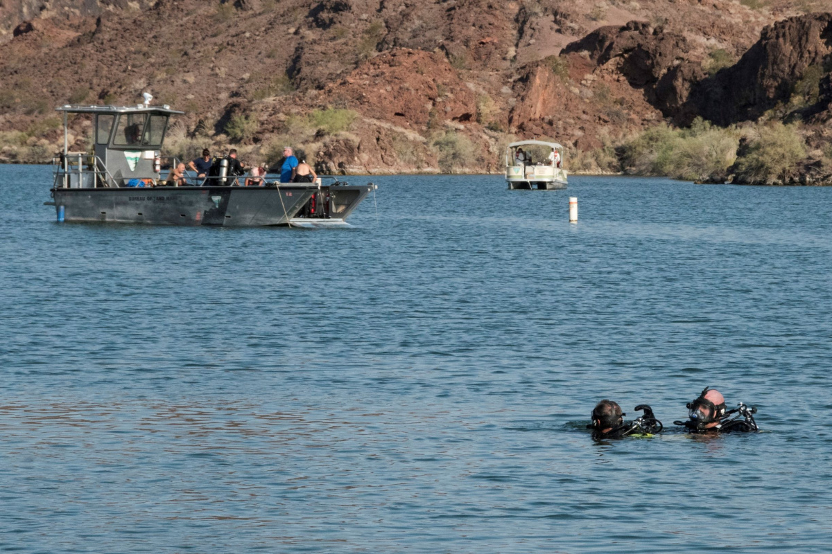 two SCUBA divers in the water with boats in the distance