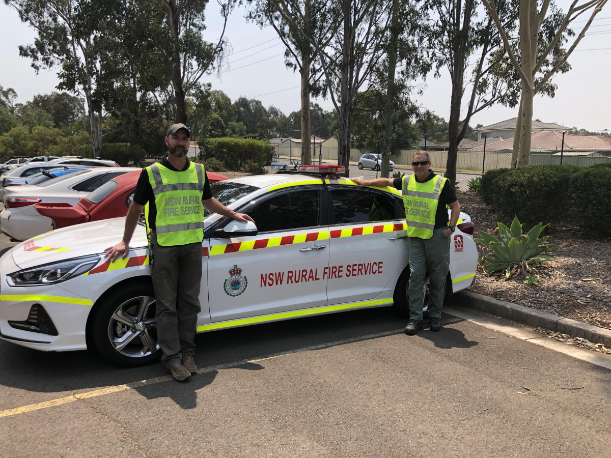 Two firefighters standing by car