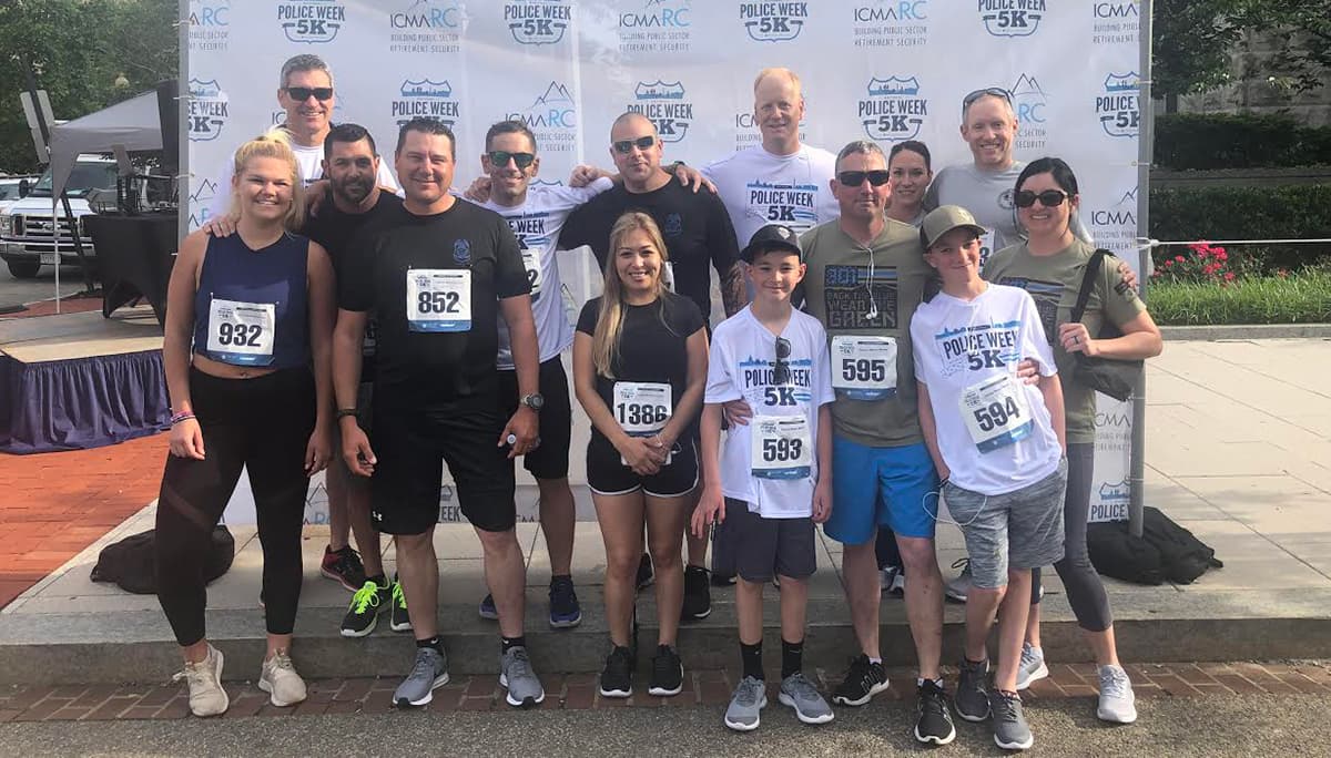 BLM Law Enforcement and their family members wearing running apparel standing in front of a background with logos for the Police Week 5K and the sponsors of the event.