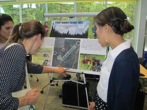 Patrice DeAsis and Jessica Mute stand next to their project posted while a woman points to an item on the poster during the ANSEP graduation reception.