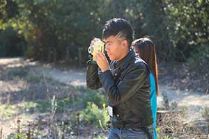 A high school student holds a camera to his face and looks through the view finder.