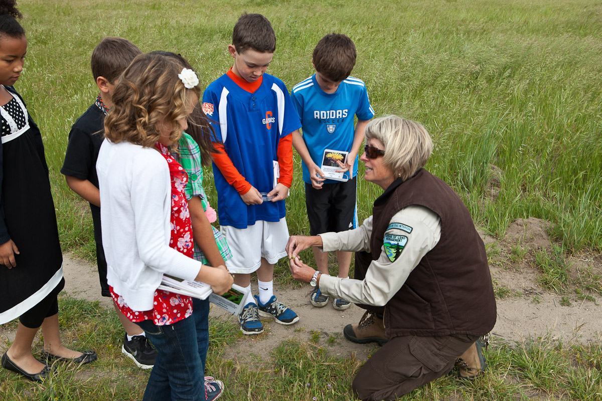 Children holding seed packets and magnifying glasses listen as a BLM employee teaches them about native plants.