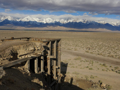 An old wooden structure on desert lands with snow-capped mountains in the distance (BLM Photo)
