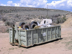A large dumpster on a dirt road is filled with trash.  Photo by BLM.