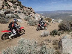 Two motorcycle riders on a dirt road leading through a mountain area overlooking a valley.  Photo by Marisa Williams, BLM.