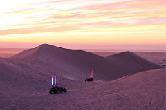 Two dune buggies ride on sand dunes at dusk.  Photo by BLM.
