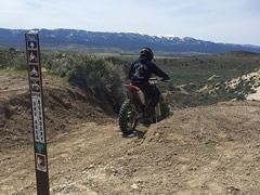 A motorcycle rider on a dirt trail rides past a sign marking the open OHV area boundary.  Photo by Marisa Williams, BLM.