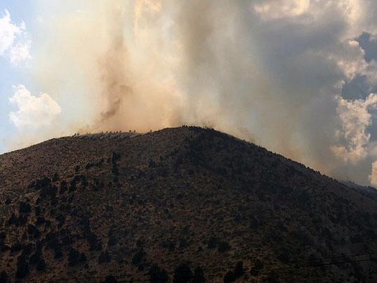 Smoke rises from a wildlife on a mountain top.  Photo by Tim Dunfee, USFS.