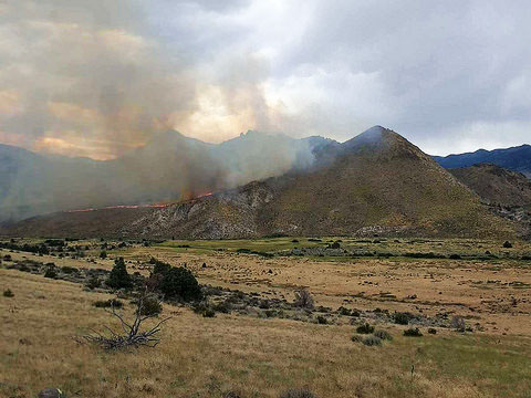 In the Slinkard Mountains, fire peaks over the ridgeline in the far distance as smoke fills the sky.  Photo by Troy Maguire, BLM.