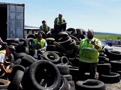 A group of people stand and sit in a pile of tires collected for recycling.  Photo by Georgette A. Fogle, BLM