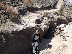 A person stands in a deep washed out area of a dirt trail.  Photo by BLM.