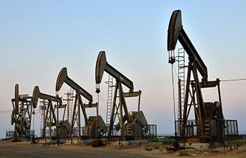 A group of people in BLM uniforms and hard hats standing next to a BLM truck in front of a pump jack.