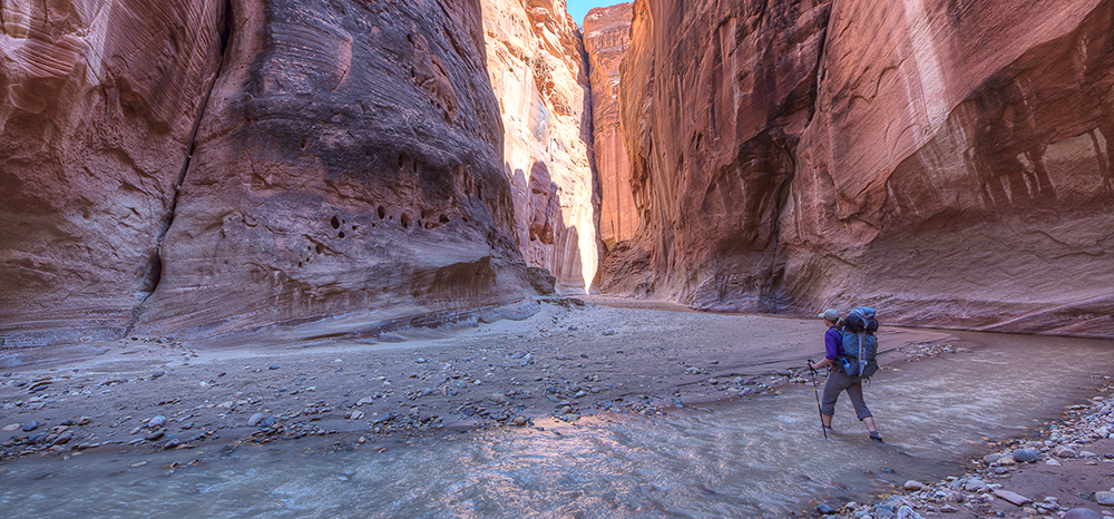 a hiker stands in running water beneath massive vertical cliffs