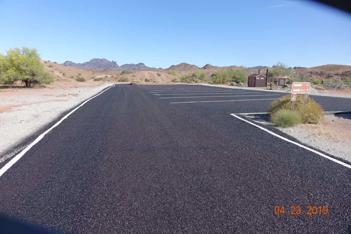 Recently paved parking area with restroom facility in background.