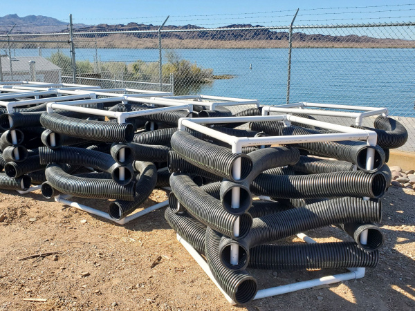 metal cubes holding black PVC pipe sit near a lakeshore