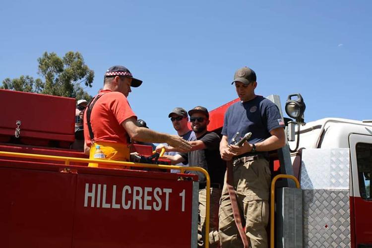 Four wildland firefighters perched on the back of an Australian fire engine