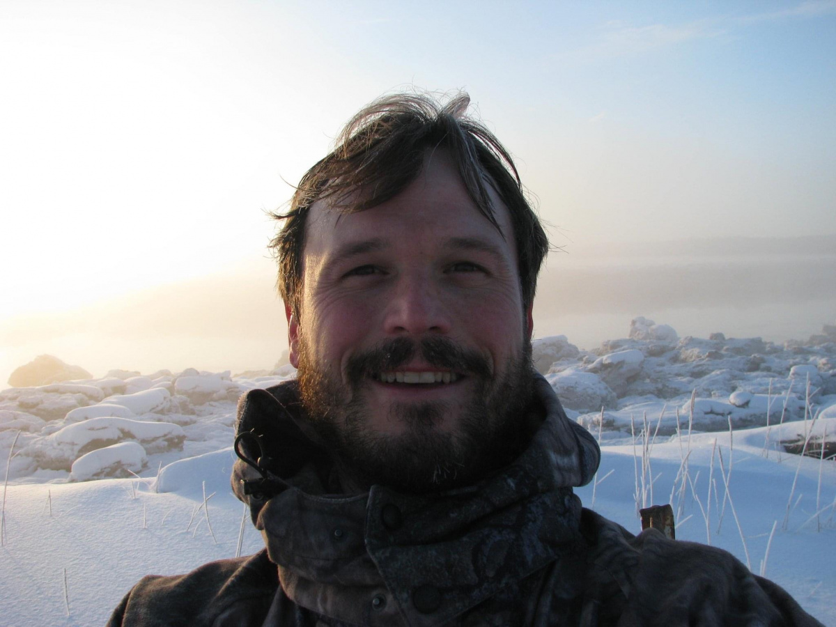 A man takes a selfie outside during winter, the sun is glowing through fog behind him.