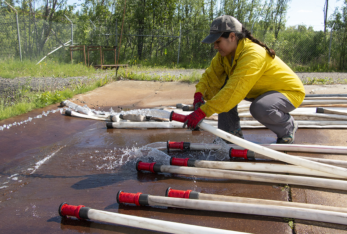 Worker holding a fire hose with water coming out.