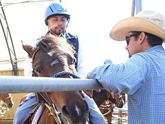 A man holds a horse against a metal fence while a trainer in a helmet sits horseback. Photo by Jeff Fontana/BLM.
