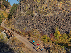 And Arial shot of bikers on a trail with a bridge in the background. 