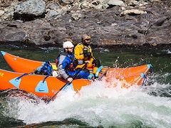 Two rafters shoot difficult rapids in a rocky river.