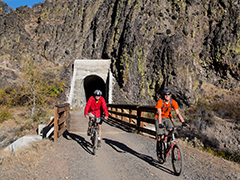 Bikers on a trail in front of a tunnel. 