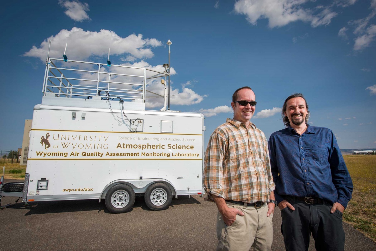  Two men stand in front of a large white trailer.