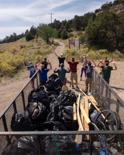 college students stand behind a trailer filled with trash bags and garbage