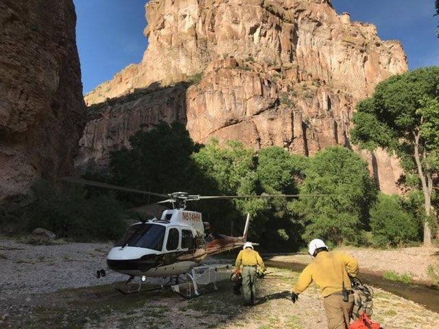 Weaver Mountain helitack firefighters carry equipment toward helicopter in Aravaipa Canyon landing zone.