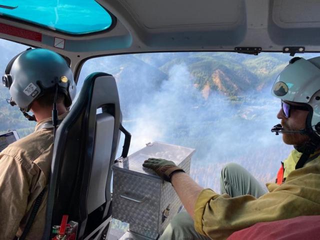 Weaver Mountain Helitack in helicopter operating a plastic sphere dispenser over a wildfire 