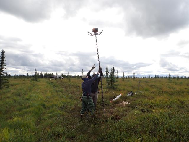 Two men lowering a power auger into a hole.