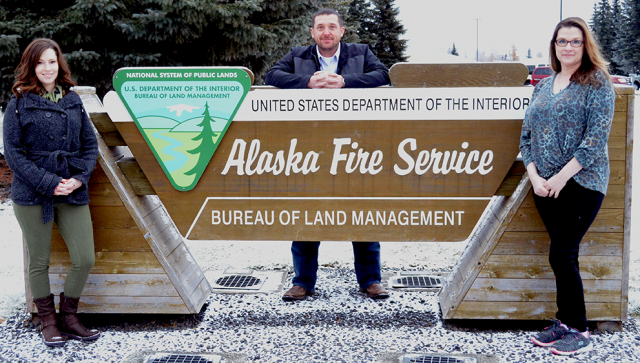 Three people standing by Alaska Fire Service sign