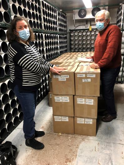 A man and a woman stand with neatly stacked and sealed cardboard boxes.