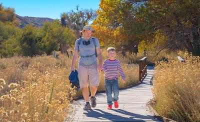 Father and son walk on a board walk in a nature preserve.
