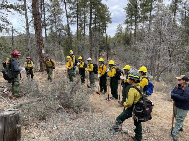 Wildland firefighters stand in a single file line at the Women in Wildfire bootcamp facing an instructor and receive instruction 