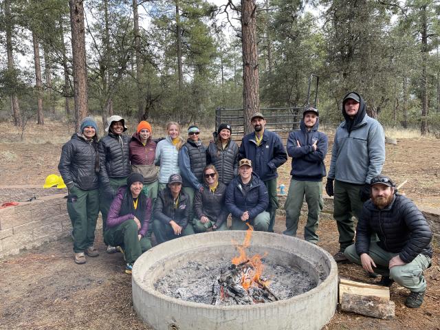 Participants in the Women in wildfire boot camp posed around a large mental campfire ring with a campfire. 
