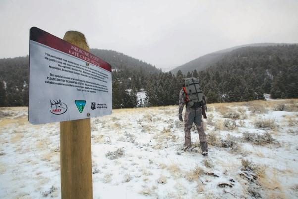snowy white public lands sign with hiker going into the distance